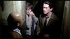 Three people are depicted in a dimly lit scene inside a narrow passage. A bald man with his back to the viewer faces two individuals, one holding a flashlight. The person in the center looks concerned, while the man on the right appears serious and thoughtful.