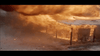A large dust storm sweeping through a desert area, obscuring visibility. The sky is filled with a thick cloud of dust and sand, making the environment appear ominous and chaotic. In the foreground, structural elements of a shelter or building are partially visible.