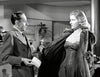 A man in a suit talks to a woman in a strapless dress and fur coat in a chic setting, echoing 1940s Hollywood glamour—a scene captured in the classic film "Caught (1949)" now available on DVD.