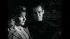 A woman and a man sit together in a car at night, illuminated by dramatic lighting. This striking black-and-white scene evokes the timeless allure of Caught (1949) DVD, a rare gem from Hollywood's golden era.