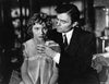 A black-and-white scene from "Caught (1949) DVD" evokes classic Hollywood: a suited man gently hands water to a worried woman in a sheer robe, all set in a dimly lit, vintage-decorated room.