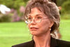 An older woman with gray hair, glasses, and pearl earrings gazes outdoors in a dark blazer—evoking classic Mary Tyler Moore, as seen in the rare movie "A Most Deadly Family (2001) DVD" against a soft-focus green background.