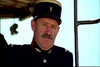 A man in a dark military uniform and flat-topped hat with a red and gold band stands outside, looking serious against a bright sky—reminiscent of scenes from the March or Die (1977) DVD.