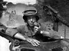 A soldier in a helmet uses a radio from a military vehicle, with another following on a dusty tree-lined road—imagery reminiscent of scenes from the classic film "The Tanks Are Coming (1951)" DVD.