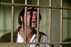A man with a concerned look stands behind prison bars, shadows lining his face. Dressed in a light shirt, he gazes out from a jail cell—evoking scenes from classic films like Moon of the Wolf (1972) DVD.