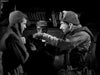 Three men in rugged clothing engage in a tense exchange in a dimly lit room—one points accusingly while another appears defensive. Experience this gripping scene and more with the Time Limit (1957) DVD, now available.