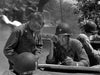 Three soldiers in uniform study a map on a jeep—one using a radio—with blurred tanks and troops in action behind them. Ideal for fans of classic war films, The Tanks Are Coming (1951) DVD captures the excitement of battlefield strategy.