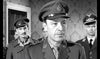 Three men—two in British and one in German military uniforms—stand indoors in this striking black-and-white WWII drama, The One That Got Away (1957) DVD. The front man appears serious while the others look alert. Ideal for classic film fans.