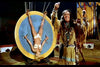 A man in Native American-style costume stands by a large spinning target with a woman strapped upside down, reminiscent of scenes from vintage films like Circus of Horrors (1960), now available on DVD.