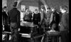 A group of men in military uniforms and civilian clothes gather in a room—perfect for fans of WWII drama, this tense scene is from "The One That Got Away (1957) DVD.