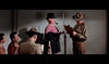 A man in a pink outfit with a pipe and stick stands before two uniformed officers with a clipboard—an iconic moment reminiscent of The Long Gray Line (1955) DVD—while two shirtless men sit nearby against a tiled wall.