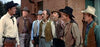 Seven men in cowboy hats and western attire stand outside a brick building, resembling a scene from classic films like The Oklahoman (1957) DVD.