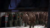 Rows of similarly dressed boys in plaid coats and hats stand near green barrels in a dark, industrial setting, creating an eerie mood reminiscent of a sci-fi film like the Screamers (1995) DVD. The scene is shadowed by a large overhead structure.