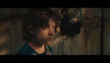 A young boy with wavy brown hair stands indoors, looking serious as an old rotary phone hangs on the wall behind him—a moody scene evoking a thriller, featured on The Black Phone (2021) DVD cover.