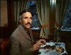 A mustachioed man in a suit dines by a curtained window in a dim dining car as snowy scenery passes—a scene evoking moments from the Horror Express (1972) DVD.
