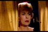 A woman with short blonde hair and red lipstick stands between yellow curtains, her serious gaze evoking vintage drama—reminiscent of scenes from Circus of Horrors (1960) DVD.