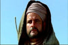 A man with a short beard and mustache, wearing a tan turban and hooded robe, stands outdoors under a clear blue sky—evoking the serious, thoughtful scenes found in the classic film March or Die (1977) DVD.