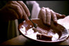A close-up of hands using a spoon to scrape fish on a brown plate, softly lit and focused on dining—capturing intimate details much like those seen in Effigy: Poison in the City (2019) DVD.