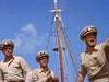 Three men in khaki naval uniforms stand alert on a ship with a tall mast behind them—a memorable scene from The Sharkfighters (1956) DVD, ideal for rare movie collectors.