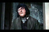 A man with a swollen, closed eye stands before a stone wall in a dark coat and scarf, his solemn gaze evoking the haunting mood of "Blood of the Vampire DVD (1958).