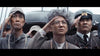 Three men salute in the foreground—one in a navy uniform, two in civilian clothes—in a scene from the Godzilla Minus One (2023) DVD; more people and a ship appear blurred in the background.