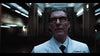 A man in a white lab coat and dark-rimmed glasses stands in a dimly lit, futuristic hallway—evoking a supernatural vibe—reminiscent of scenes from the Haunting of Queen Mary (2023) DVD.