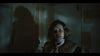 A frightened girl stands indoors, dimly lit with a looming shadow behind her, capturing the suspenseful atmosphere of a supernatural tale in "Haunting of Queen Mary (2023) DVD.