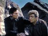 Two men in dark clothing sit on rocky terrain, one resting his hand on the other's shoulder, appearing as serious western characters. This scene evokes the atmosphere of "Kentucky Rifle (1955) DVD," with looming rock formations under a clear sky.