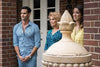 Three people stand outside a brick building and a stone structure—just like a scene from "Murder at the Mansion (2018) DVD," a rare find that true crime fans treasure.