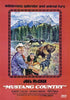 A cowboy and a Native American child stand together in the wild, while a bear pursues a black mustang in the background of majestic mountains and towering trees. Above them, the text reads: "Wilderness splendor and animal fury—capturing the spirit of a classic Western adventure that makes Mustang Country DVD a family-friendly favorite.