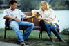 A man and woman sit on a bench by a lake, yellow tape linking their waists—a scene reminiscent of the heartfelt moments in "Nothing in Common (1986)" DVD, as he gazes thoughtfully at her while she wraps the tape around them.