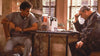 Two men share a kitchen table—one thoughtful, one relaxed. A cereal box and coffee sit nearby as sunlight streams in, evoking scenes from classic films like the "Nothing in Common (1986) DVD.