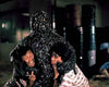 A chilling scene evocative of Hong Kong horror DVD covers and the eerie ambiance of Asian cult cinema: on the Oily Maniac (1976) DVD, a creature coated in black, gooey slime seizes two terrified individuals—one on each side—in a dimly lit, industrial environment scattered with barrels in the background.