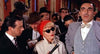 A woman in sunglasses and a red hat stands between two men in suits—one holding a microphone—amidst a crowd, some wearing hats, at what appears to be a bustling indoor event for "Gorgo (1961) DVD" collectors or fans of rare classic monster movies.