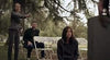 A woman points a gun while two people sit on white folding chairs outdoors among trees, in a tense scene from the rare life-after-death movie We Go On (2016) DVD.