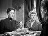 Three women sit around a table set for tea in a Victorian-era room, evoking the refined atmosphere found in rare films. Two women face the camera—one solemn, one attentive—while the third sits with her back to the viewer. The scene captures an air of timeless elegance reminiscent of “The Ghost and Mrs. Muir (1947)” on DVD.