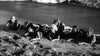 Seven people lie on a sandy beach near the water’s edge, echoing classic scenes from "Saga of the Viking Women (1957)"—now available on DVD. Ocean waves roll in the black and white background, evoking rare cinematic adventure.
