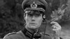A man in military uniform and peaked cap holds a telephone to his ear with a serious look, evoking classic WWII films. This black-and-white image is from the "Screaming Eagles (1956) DVD.
