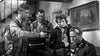Inside a tense room, four uniformed individuals face off—one man points a gun at another on the phone, while a woman holds wires and another man stands behind. Relive this WWII drama with the "Screaming Eagles (1956) DVD.