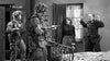 Two soldiers in uniform aim weapons at a man with raised hands as a woman stands by in a bedroom—a dramatic scene from “Screaming Eagles (1956)” DVD, echoing the WWII action of the 101st Airborne Division.