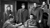 Inside a wooden barracks, six men in military uniforms––four standing, two playing cards, one on the top bunk––evoke classic WWII film tension in this scene from Screaming Eagles (1956) DVD.
