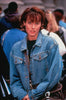 A woman with short brown hair, wearing a blue denim jacket, stands outdoors among a crowd of people, reminiscent of an extra in a classic screwball comedy—capturing the vibe of “The Counterfeit Contessa (1994)” DVD. She looks directly at the camera with a neutral expression.