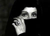 An evocative image reminiscent of a classic horror movie: a person wearing a black veil covers the lower part of their face, revealing expressive eyes and a hand adorned with a large, ornate ring—capturing the mysterious allure found in *Dracula’s Daughter (1939)*, now available on DVD.
