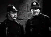 Two men in old-fashioned British police uniforms and helmets stand next to a stone wall, appearing serious. The black-and-white image evokes the atmosphere of a classic horror film—ideal for collectors looking for rare titles like Dracula’s Daughter (1939) on DVD.