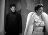 A man in a dark uniform and hat stands behind a woman in a white fur coat and evening dress, capturing an iconic scene from Dracula’s Daughter (1939) DVD. The woman’s upset expression and the man’s intense stare, set indoors with dramatic shadows on the wall, evoke the chilling atmosphere of this classic horror film.