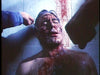 A shirtless man sits against a wall, his face and chest smeared with blood. Streaks of crimson trail down the wall behind him, while two hands—one clutching an object—emerge in the foreground. The intense, dramatic scene evokes a moment straight out of a cult horror classic like Maniac Cop, available on DVD as Maniac Cop DVD (1988).