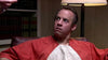A man in an orange prison uniform sits tensely on a chair, reflecting the gripping courtroom drama of "Find Me Guilty (2006)" DVD. A lamp and bookshelves with books complete the intense scene.