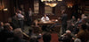 A group of men in suits convene in a dimly lit office, echoing the courtroom drama portrayed in “Find Me Guilty (2006)” DVD, where intense discussions unfold around a seated man behind a desk.