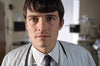 A young man in a white lab coat, dress shirt, tie, and stethoscope stands in a hospital setting, evoking Orlando Bloom’s character from The Good Doctor (2011) DVD.