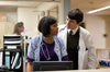 In a hospital, a female nurse in scrubs with a stethoscope stands at a desk looking away as a male doctor in a white coat—similar to The Good Doctor (2011) DVD—stands beside her, seemingly talking to her.